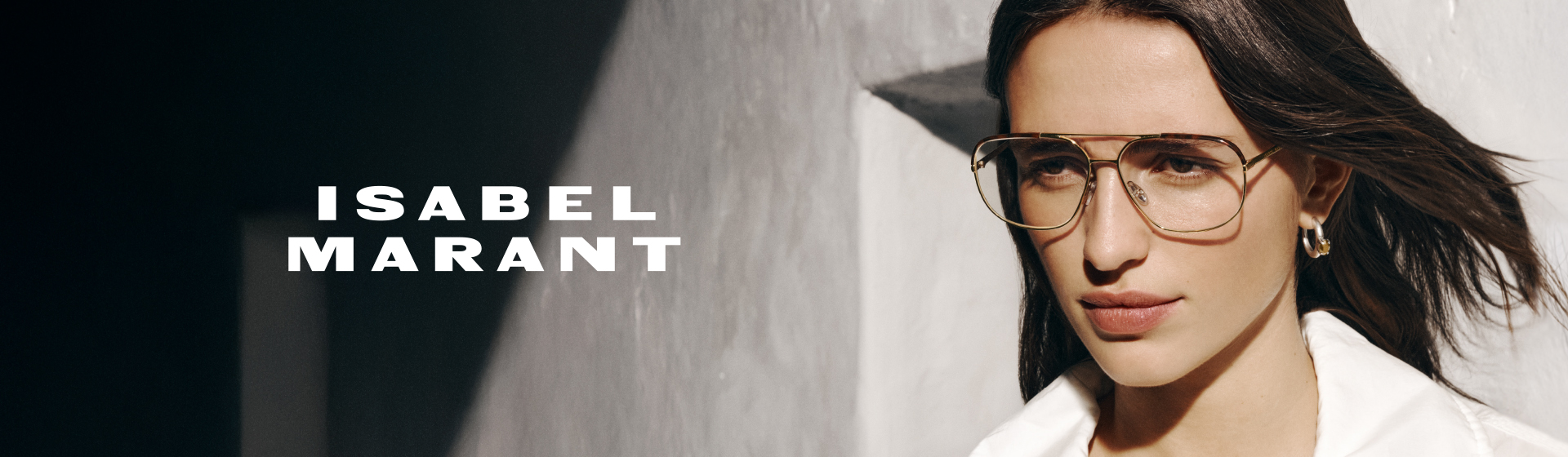 Žena s nadměrně velkými brýlemi a bílou košilí, která vrhá stín na zeď. Text na stránce zní „ISABEL MARANT”.