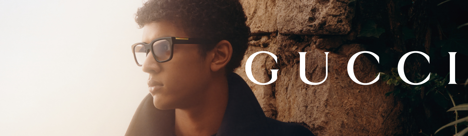 Ein Mann mit Brille und dunklem Mantel, die zur Seite schaut, mit der Aufschrift „GUCCI”.