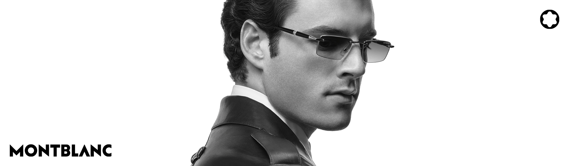 Mann mit Sonnenbrille und Anzug schaut zur Seite. Montblanc-Logo und Stern-Emblem sind zu sehen. Schwarz-Weiß-Bild.