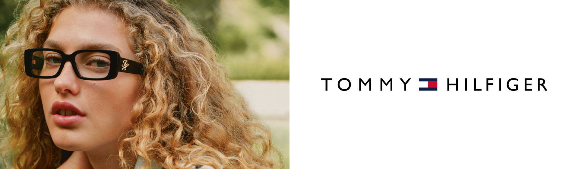 Una persona con i capelli ricci indossa occhiali rettangolari all'aperto. È visibile il logo Tommy Hilfiger.