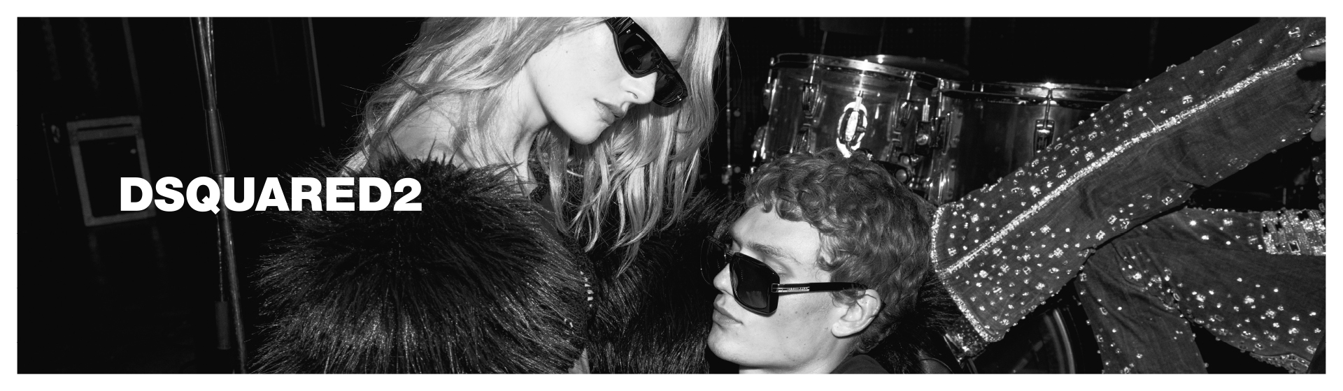 Černobílá fotografie dvou osob v elegantním oblečení a slunečních brýlích. S logem „DSQUARED2”.