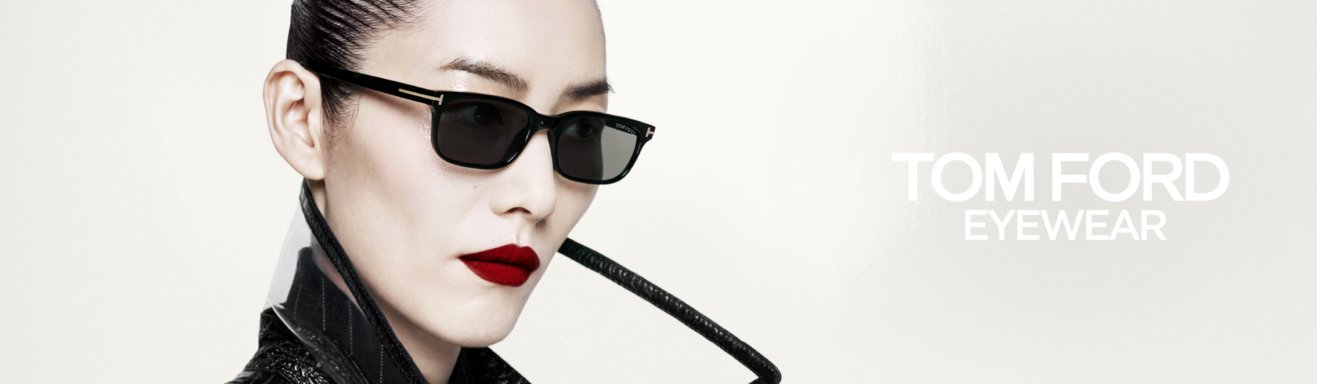 Osoba w czarnych okularach przeciwsłonecznych i z czerwoną szminką, ubrana w elegancki czarny strój, z napisem „Tom Ford Eyewear” na białym tle.