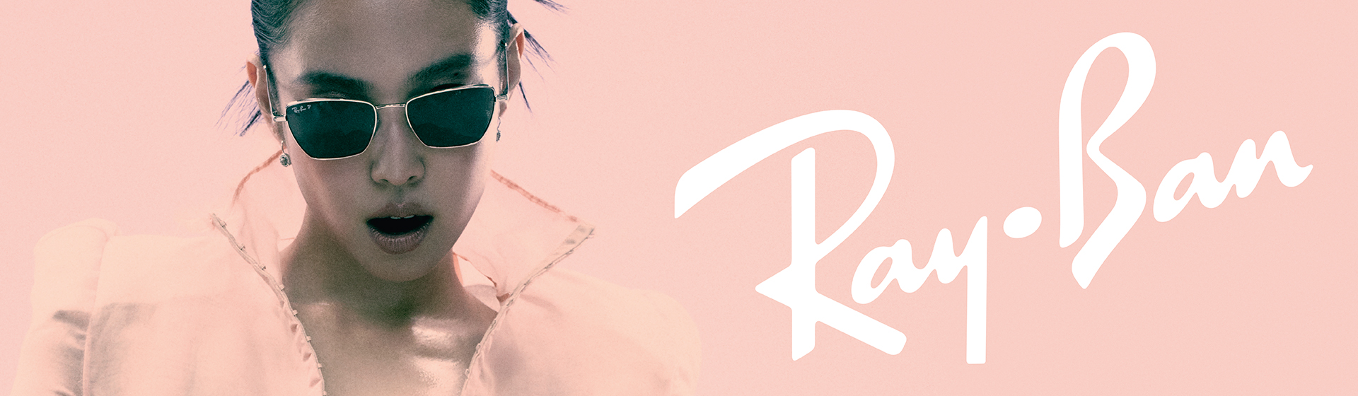 Una persona indossa occhiali da sole e ha i capelli raccolti, su uno sfondo rosa. A lato è visibile la scritta “Ray-Ban”.