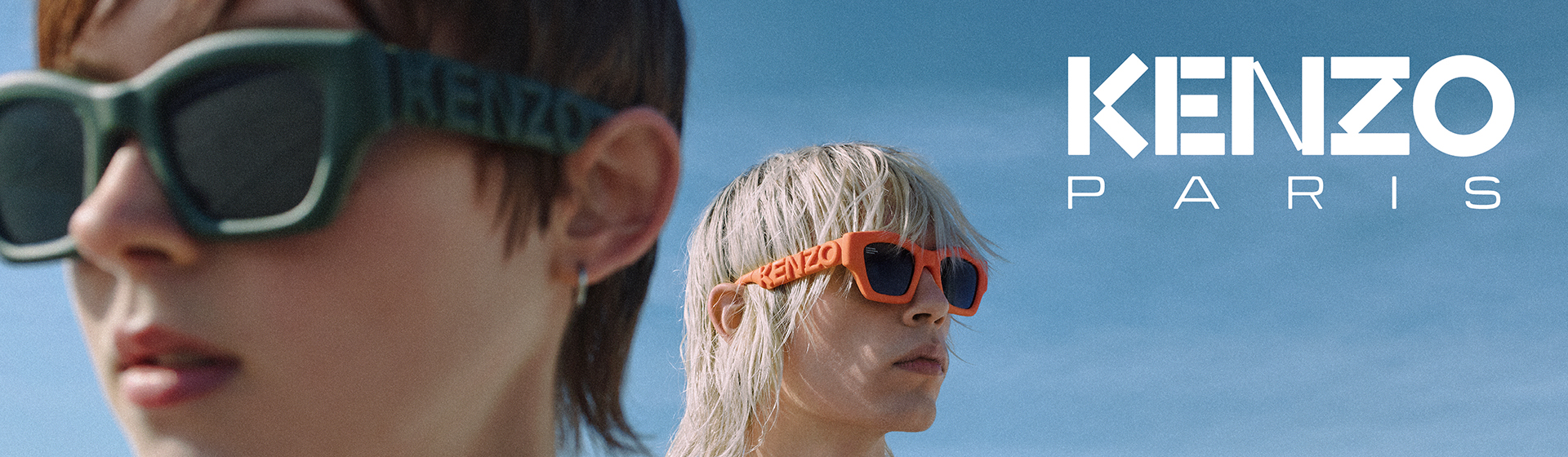 Zwei Personen tragen Kenzo-Sonnenbrillen, eine in Grün und eine in Orange, vor einem blauen Himmel. Der Schriftzug „KENZO PARIS“ ist zu sehen