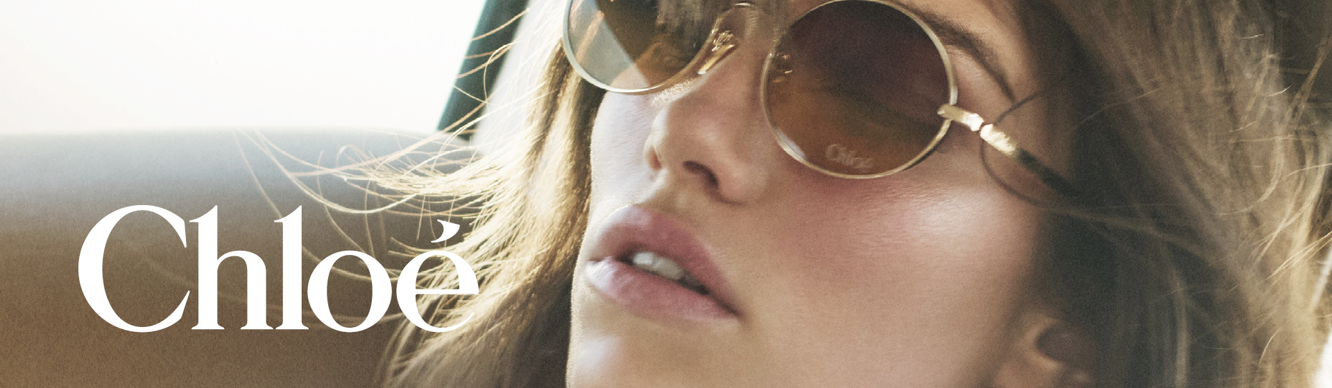 Une femme portant des lunettes de soleil et un chemisier blanc est assise dans une voiture sur laquelle est inscrit « Chloé ».