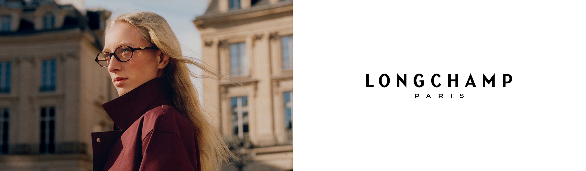 Una persona con gli occhiali e un cappotto color castagna è in piedi davanti a un edificio classico in stile europeo. A destra si vede la scritta “Longchamp Paris”.