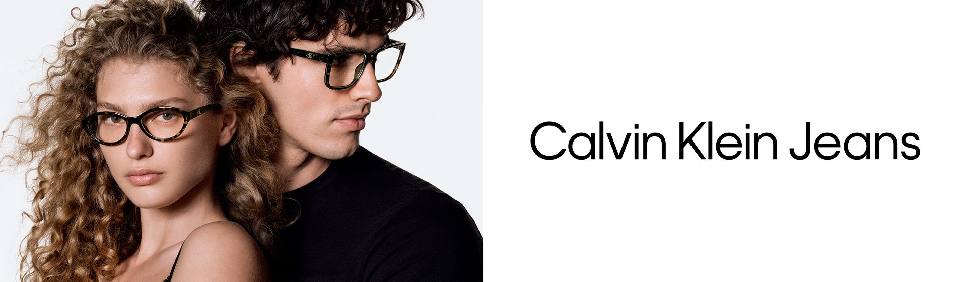 Deux mannequins portant des lunettes posent ensemble devant un fond uni. Le logo Calvin Klein Jeans est visible à droite.