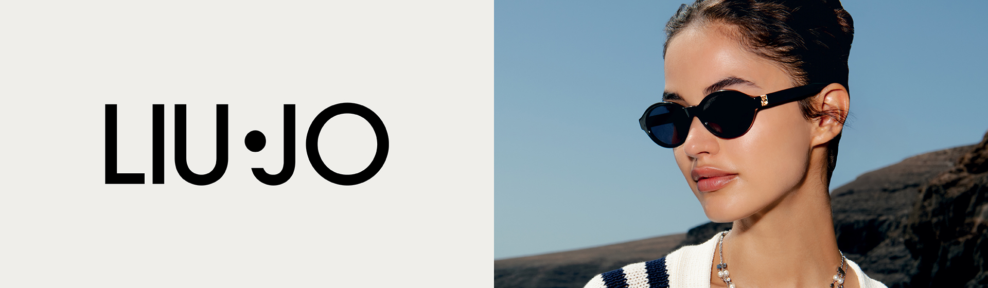 Une femme portant des lunettes de soleil et un pull rayé orné de motifs se tient au bord de la mer. On peut lire « Liu Jo ».