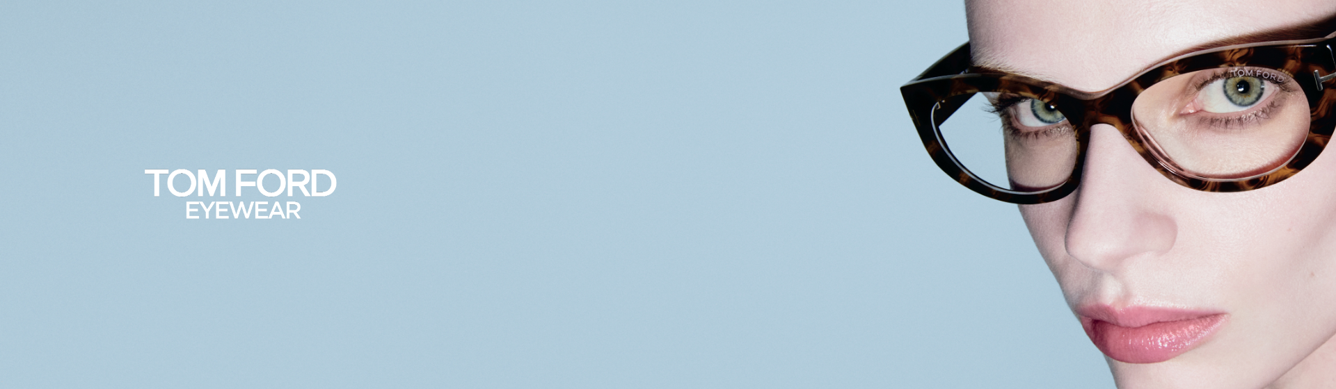 Osoba s krátkými černými vlasy, která nosí brýle Tom Ford s želvovinovými obroučkami, před světle modrým pozadím. Text zní „Tom Ford Eyewear”.