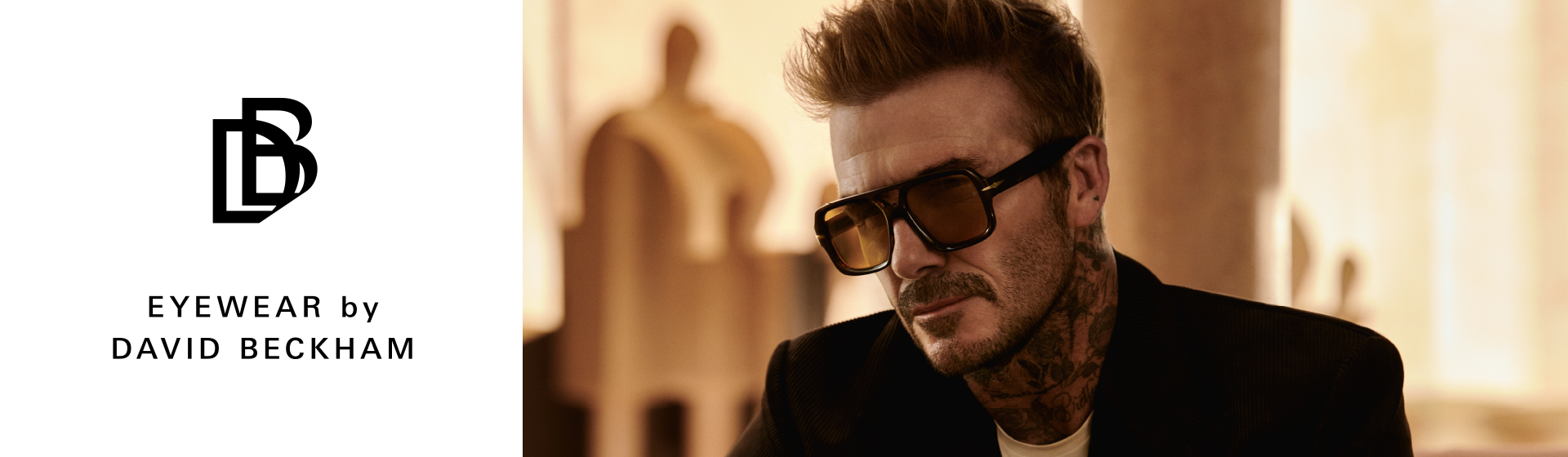 Mężczyzna w okularach przeciwsłonecznych i tatuażach, w garniturze, obok napisu i logo „Eyewear by David Beckham” na beżowym tle.