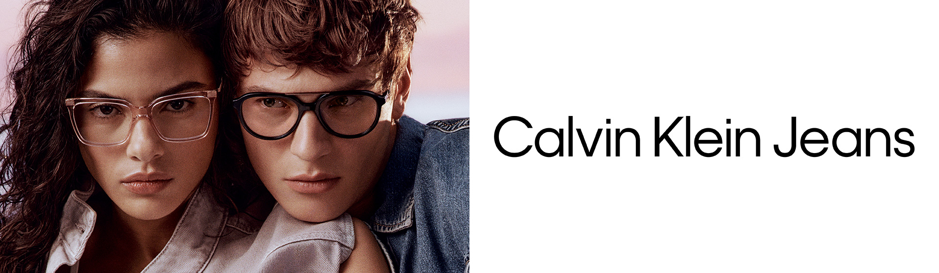 Mężczyzna i kobieta w okularach pozują blisko siebie, ubrani w kurtki jeansowe Calvin Klein. Widoczne jest logo Calvin Klein Jeans.