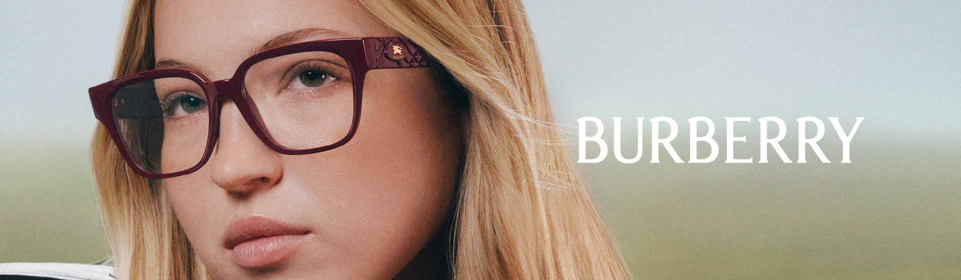 Eine Frau mit langen blonden Haaren und Brille lehnt sich an ein Autofenster; sie trägt eine schwarze Lederjacke mit dem Burberry-Logo.