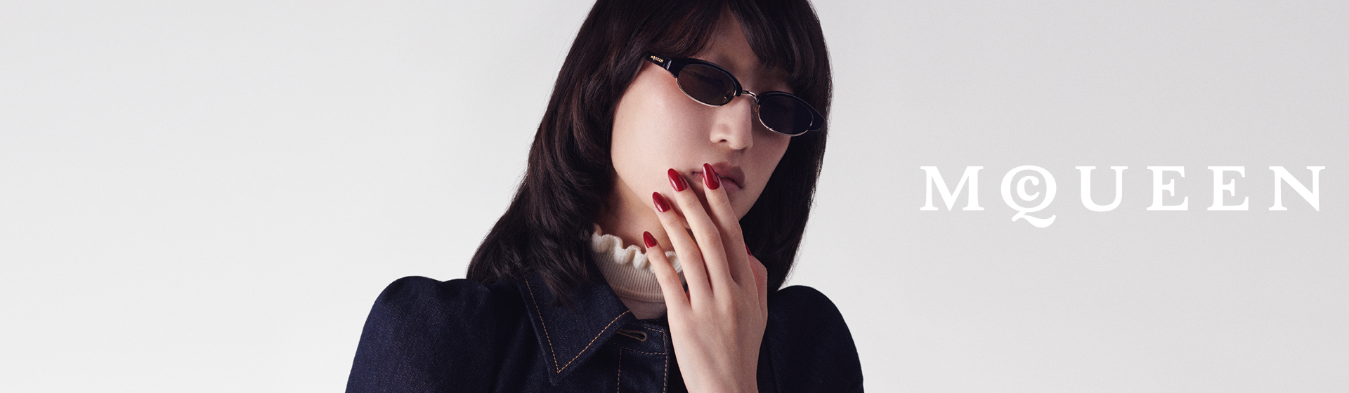 Person mit dunkler Sonnenbrille und rotem Nagellack, mit dem Schriftzug „MCQUEEN” vor einem einfarbigen Hintergrund.