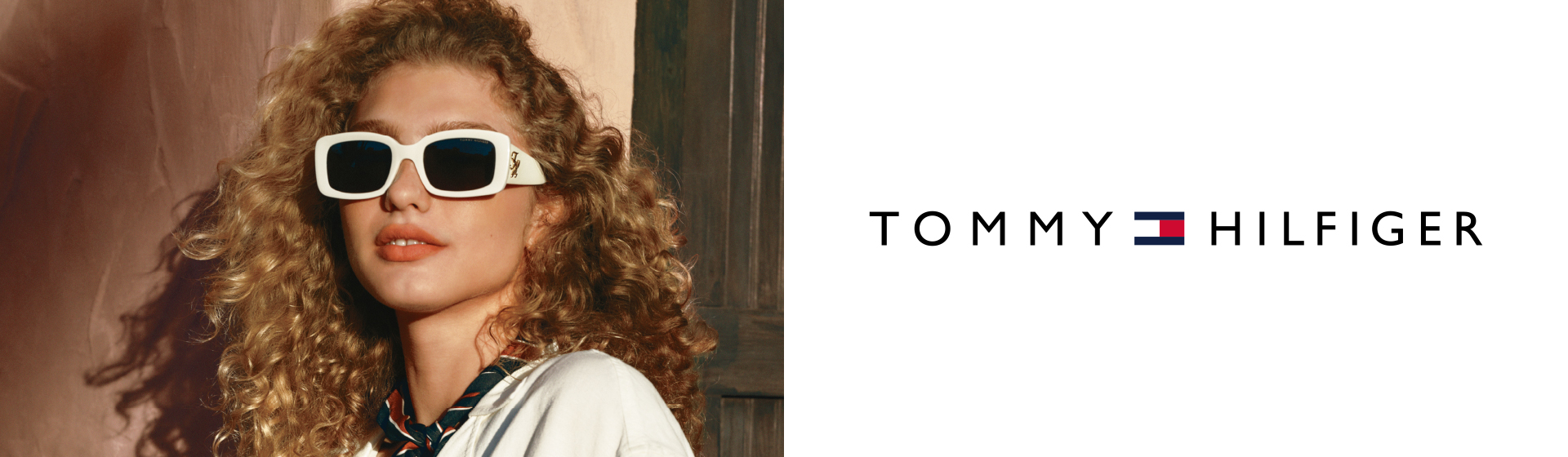Osoba o kręconych włosach, w białych okularach przeciwsłonecznych i szaliku, z logo Tommy Hilfiger z boku.