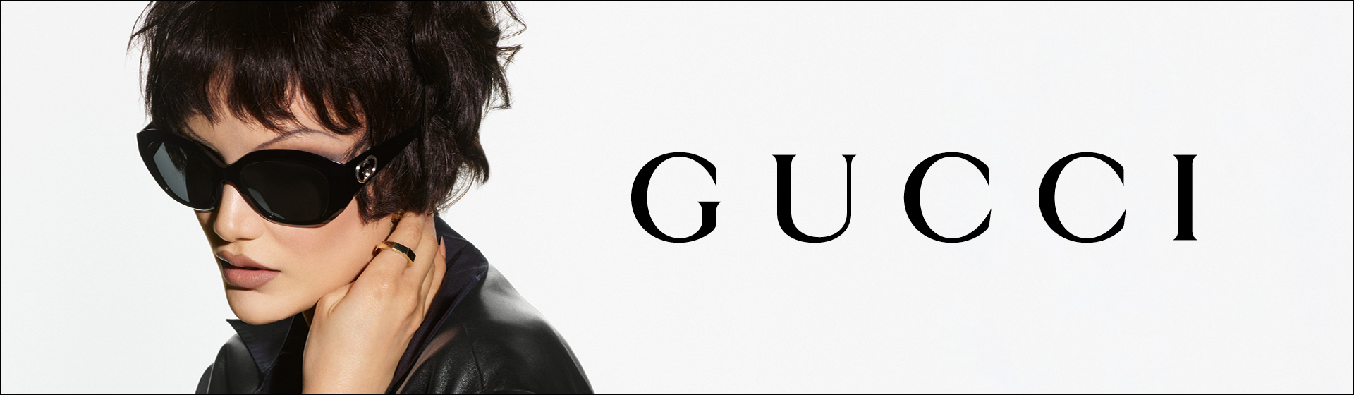 Una persona con i capelli corti, che indossa occhiali da sole neri e una giacca di pelle con la scritta “GUCCI”.
