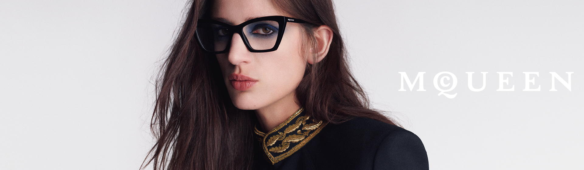 Personne portant de grandes lunettes noires et une veste brodée d'or, avec l'inscription « McQueen ».