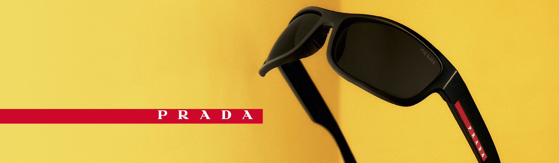 Lunettes de soleil Prada noires aux verres foncés sur fond jaune, ornées de la bande rouge portant le logo Prada sur le côté.