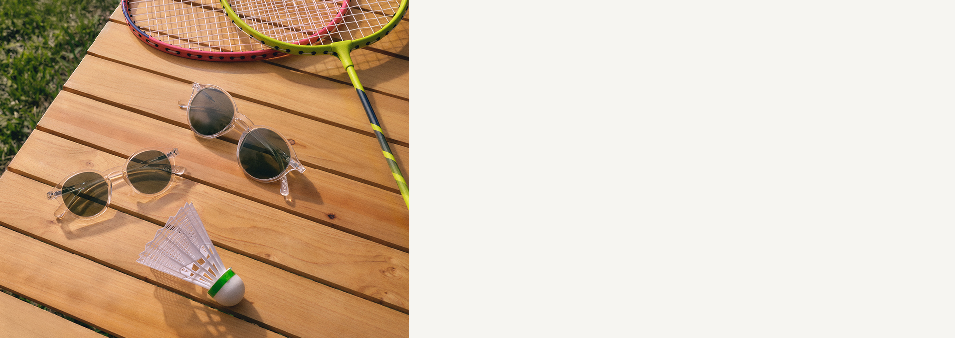 Sonnenbrillen und Federball auf einem Holztisch neben Badmintonschlägern, auf einer Rasenfläche.