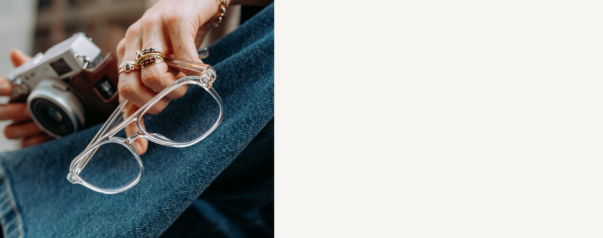 Une main tenant des lunettes transparentes et un appareil photo vintage, avec un jean bleu en arrière-plan.