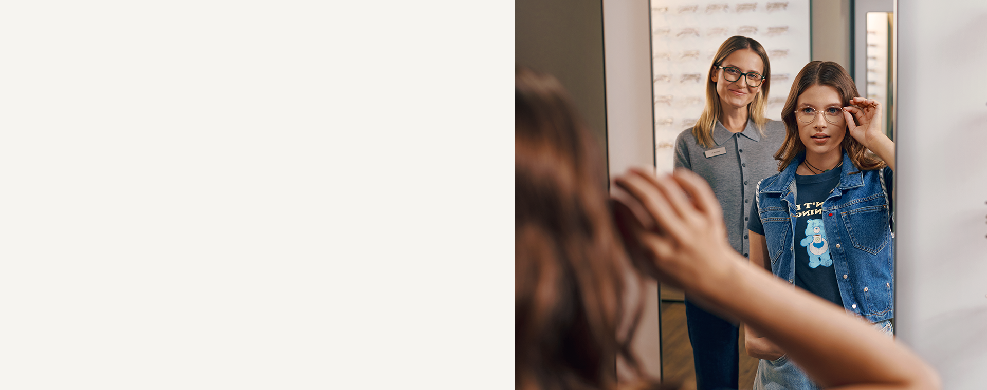 Kobieta przymierza okulary przed lustrem, a za nią stoi uśmiechnięta kobieta w profesjonalnym uniformie.