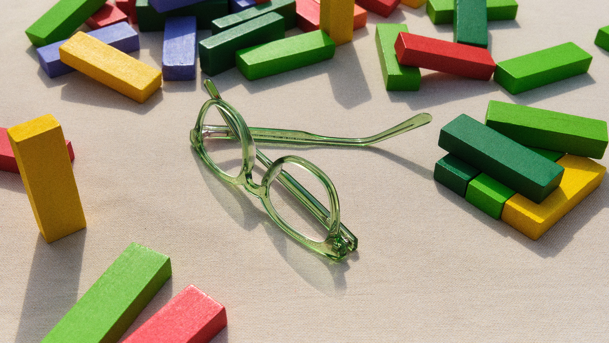 Occhiali da bambino verdi sono appoggiati su un tavolo tra blocchi di legno colorati.