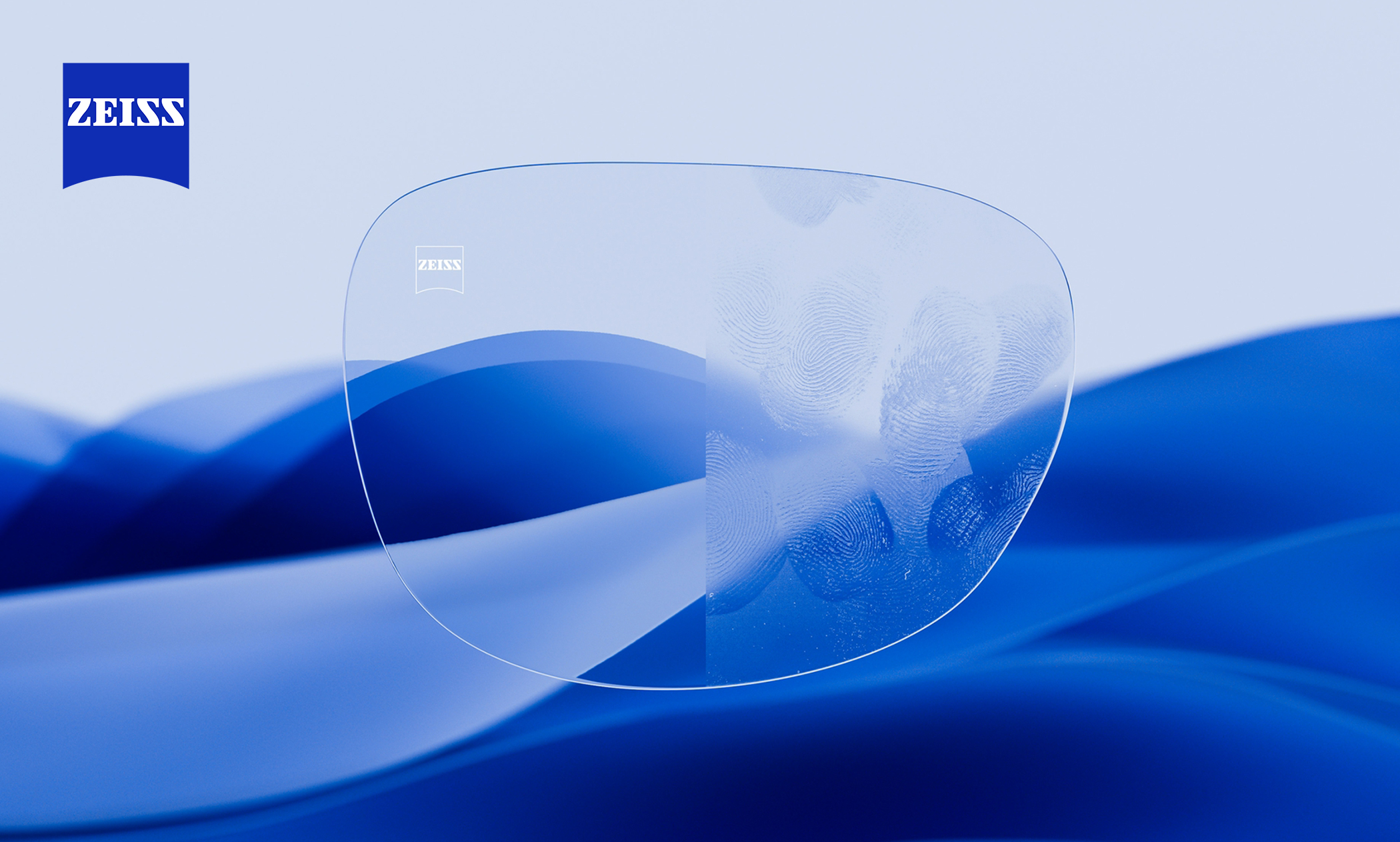 Una lente trasparente su uno sfondo blu ondulato, in parte pulita e in parte macchiata, con il logo ZEISS nell’angolo in alto a sinistra.