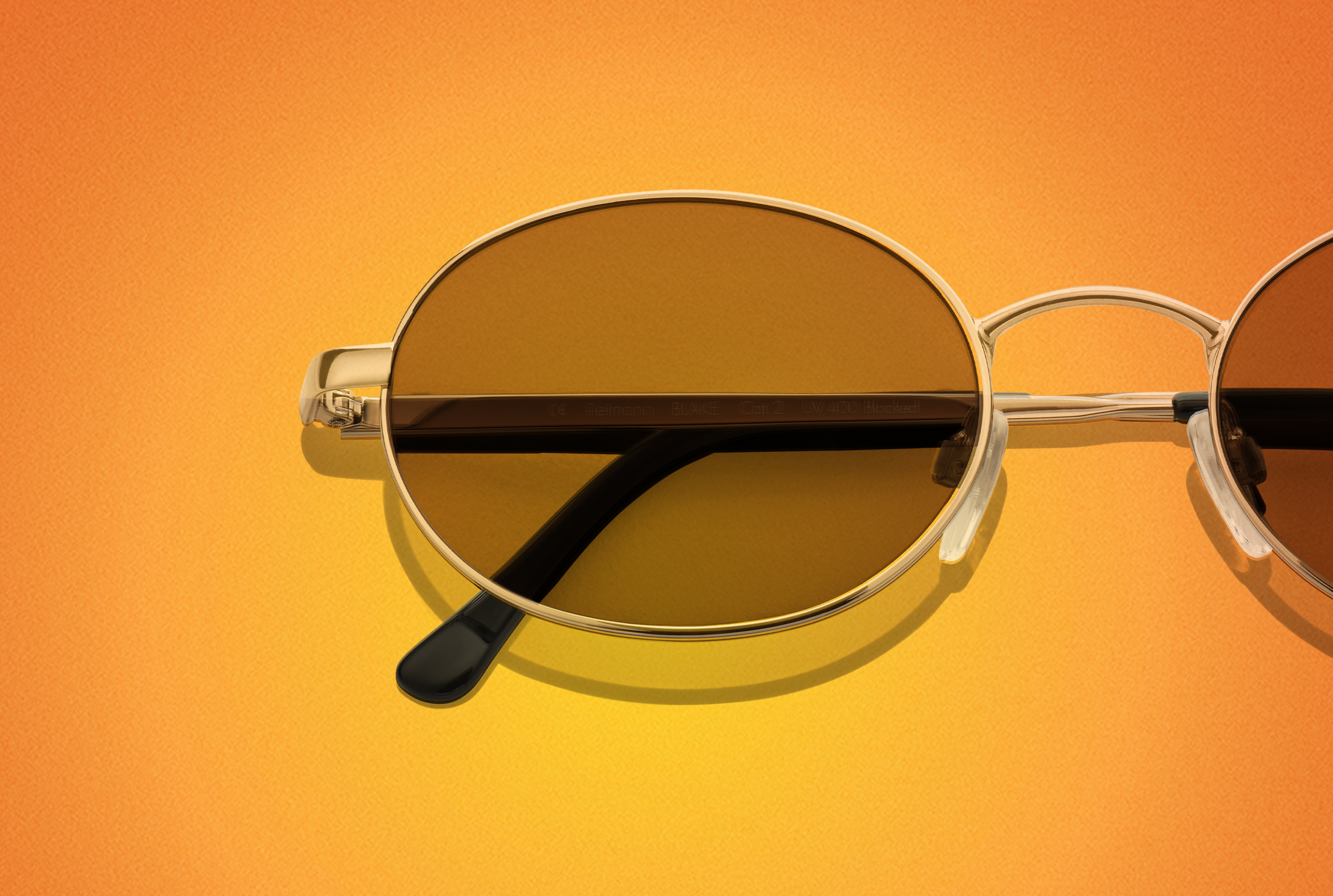 Runde Sonnenbrille mit goldenen Rahmen auf orangem Hintergrund.