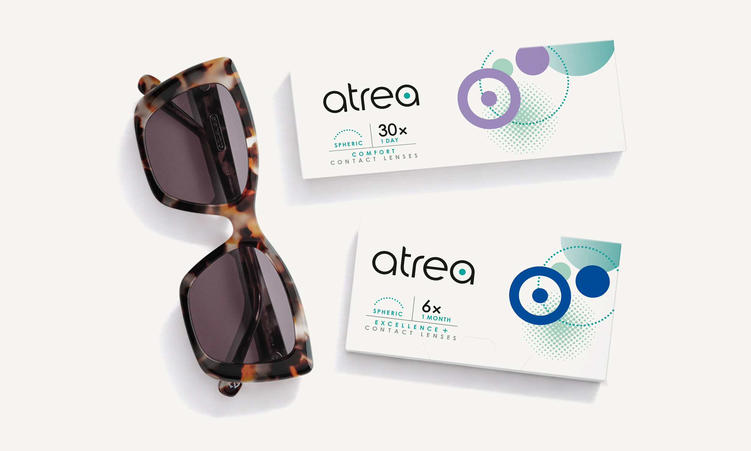 Sonnenbrille neben zwei Packungen Atrea Kontaktlinsen auf weißem Hintergrund.
