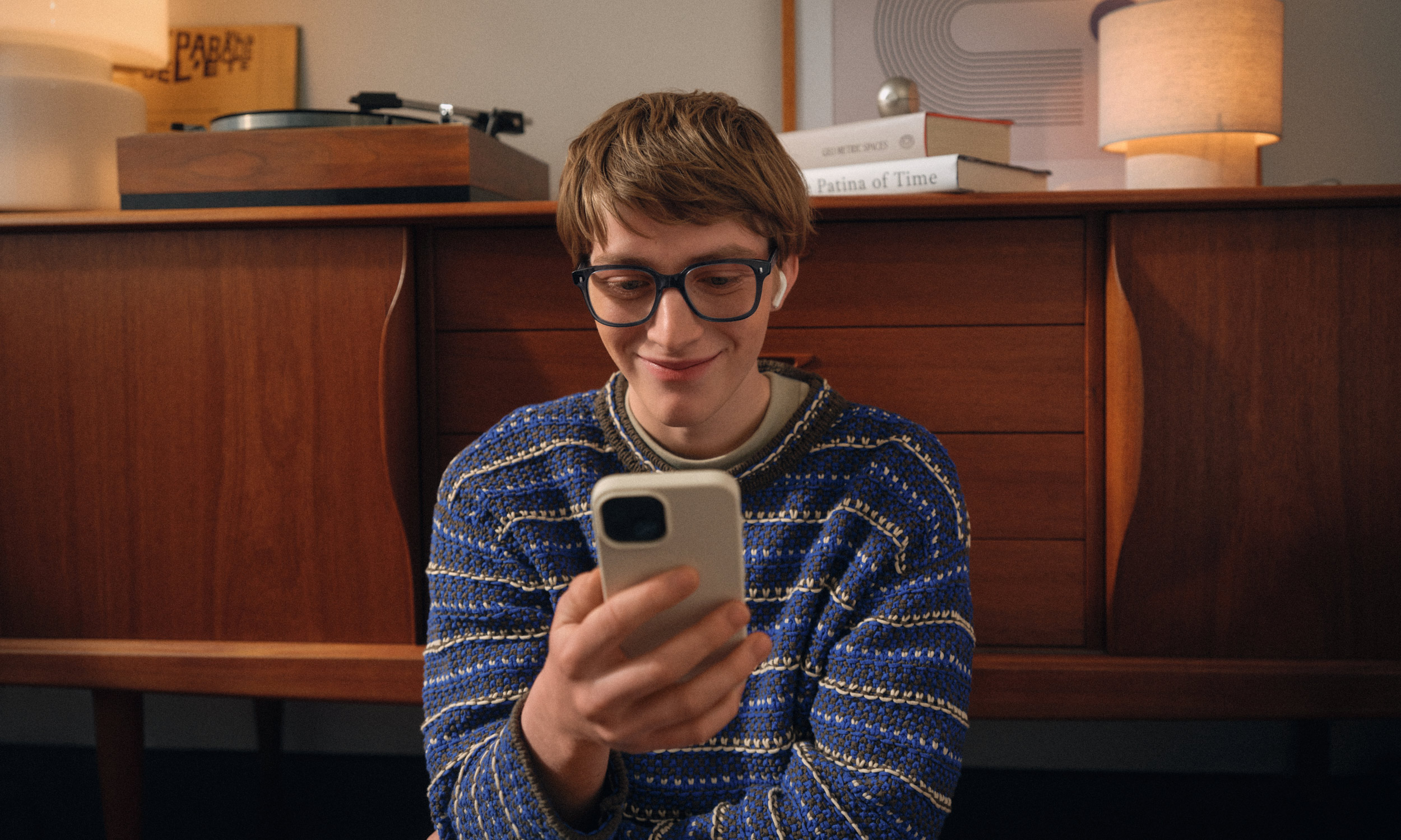 Eine Person mit Brille sitzt auf dem Boden und lächelt in ein Smartphone. Eine Person mit Brille sitzt auf dem Boden und lächelt in ein Smartphone.