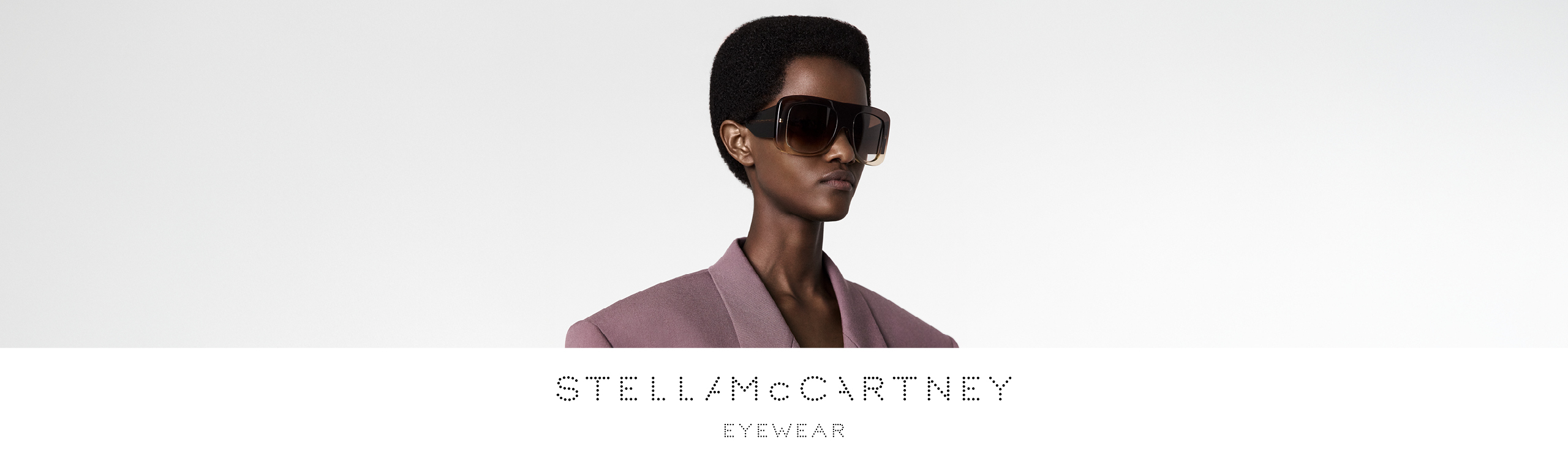 Eine Person mit übergroßer Sonnenbrille und einem mauvefarbenen Blazer vor einem einfarbigen Hintergrund. Der Text lautet „Stella McCartney Eyewear“.
