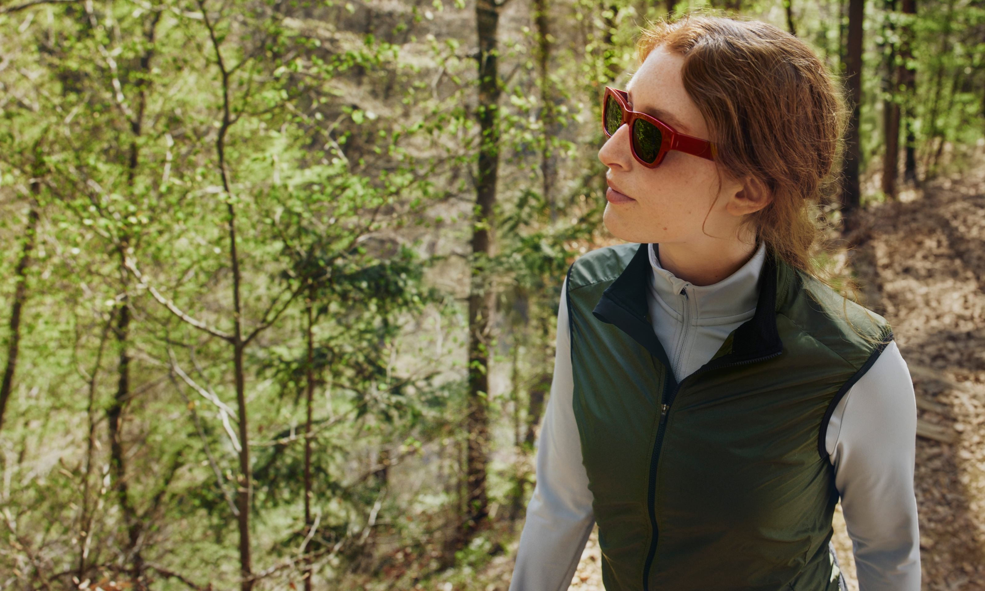 Eine Frau mit roter Sonnenbrille und grüner Weste beim Wandern.