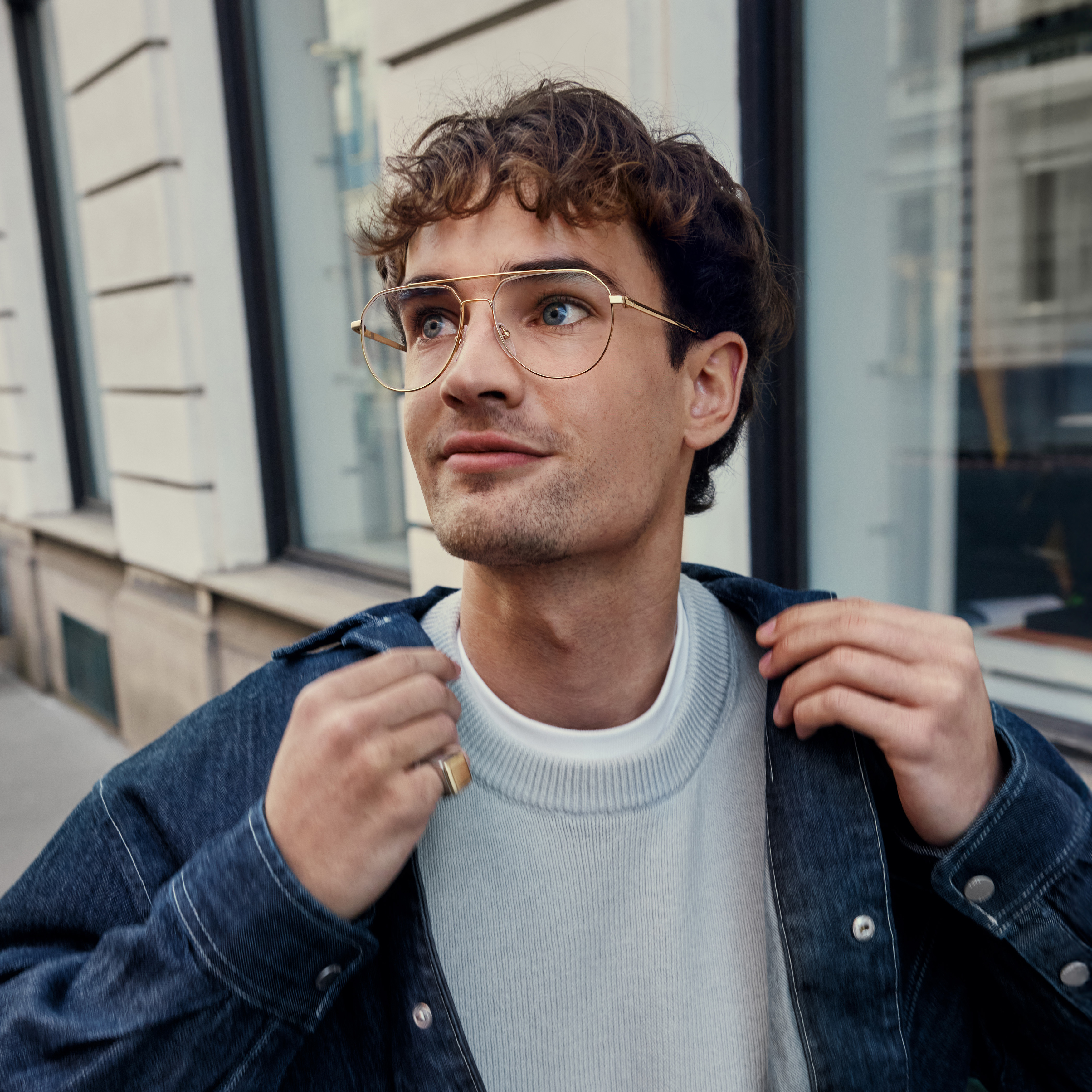 Un giovane uomo con occhiali a forma di aviator si trova davanti a un edificio.