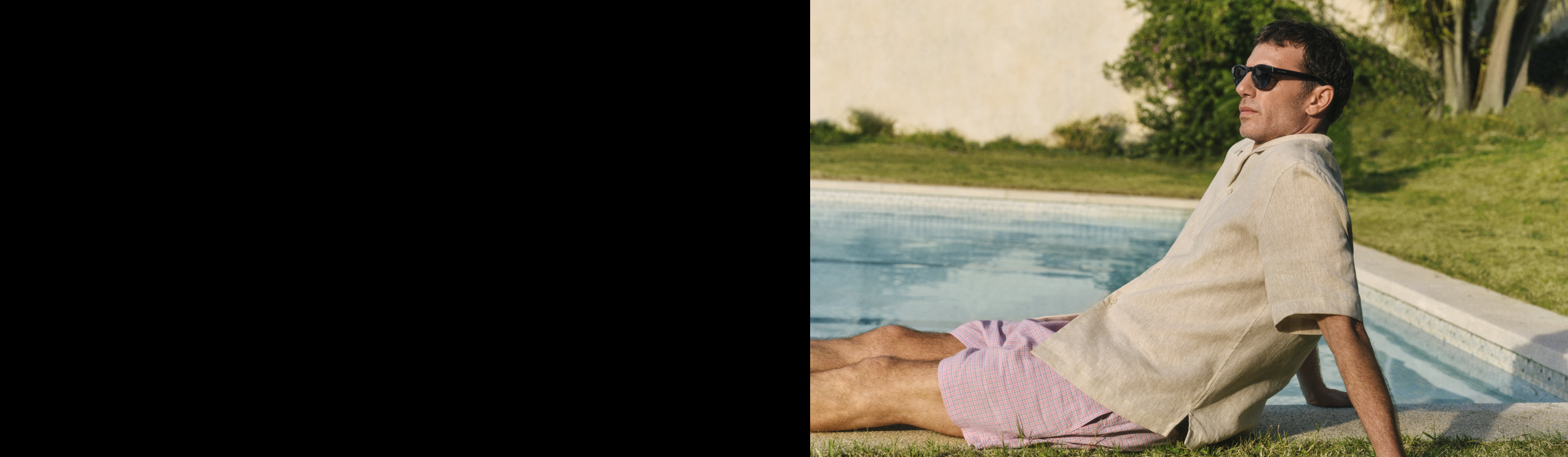 Ein Mann mit Sonnenbrille und Freizeitkleidung entspannt sich am Pool, die Hände hinter den Kopf gestützt, im Hintergrund sind grünes Laub und ein gefliester Pool zu sehen.