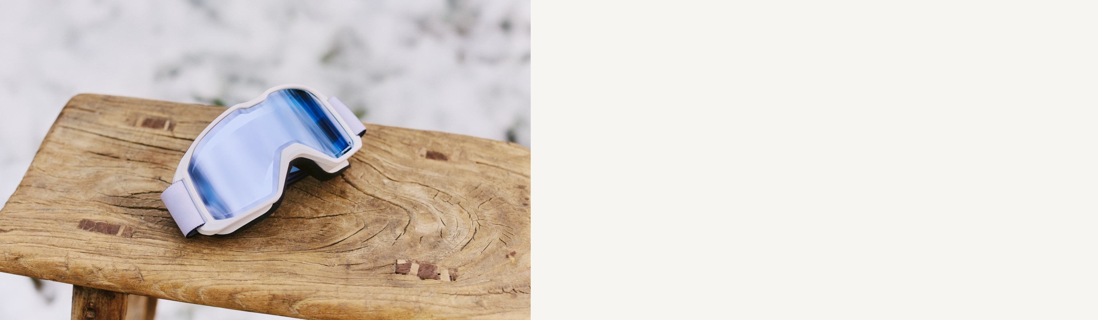 Lunettes de ski teintées en bleu posées sur un banc en bois devant un fond enneigé.