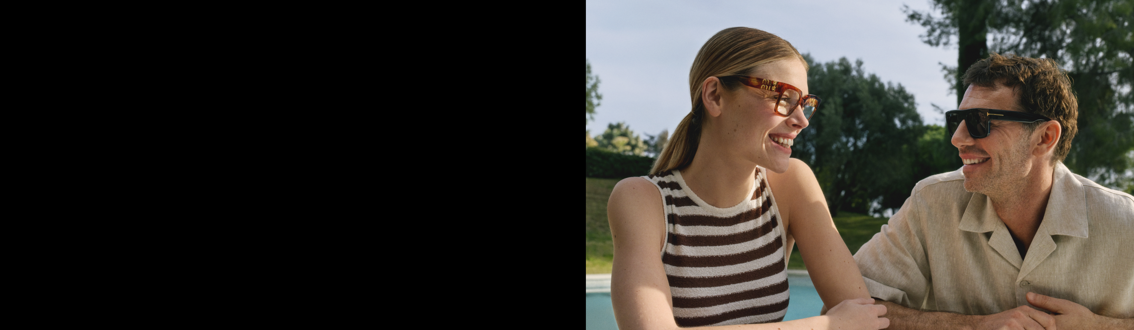 Muž a žena v slunečních brýlích sedí za slunečného dne venku a usmívají se na sebe.