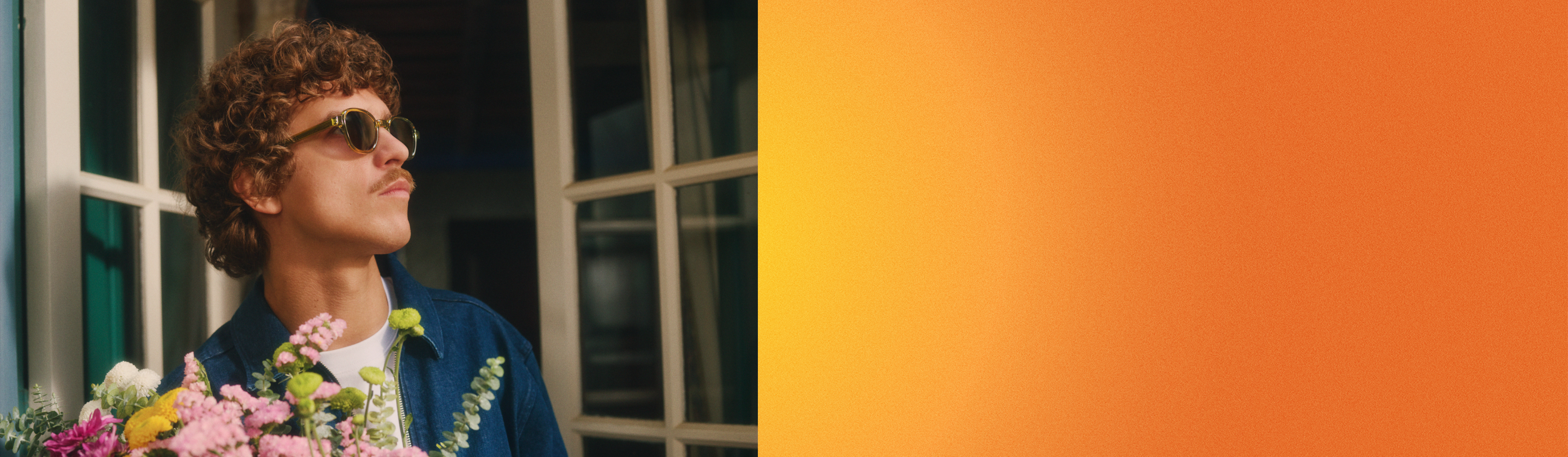 Homme aux cheveux bouclés et portant des lunettes de soleil, tenant un bouquet de fleurs colorées.