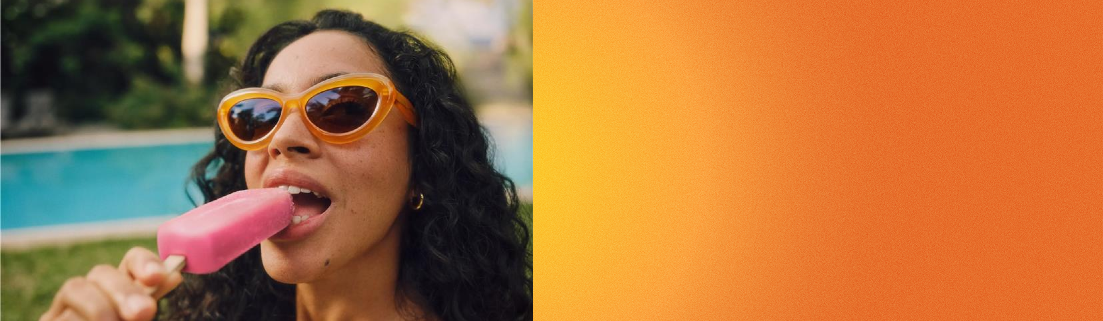 Person mit orangefarbener Sonnenbrille, die draußen ein rosa Eis am Stiel genießt, mit einem verschwommenen grünen und blauen Hintergrund.