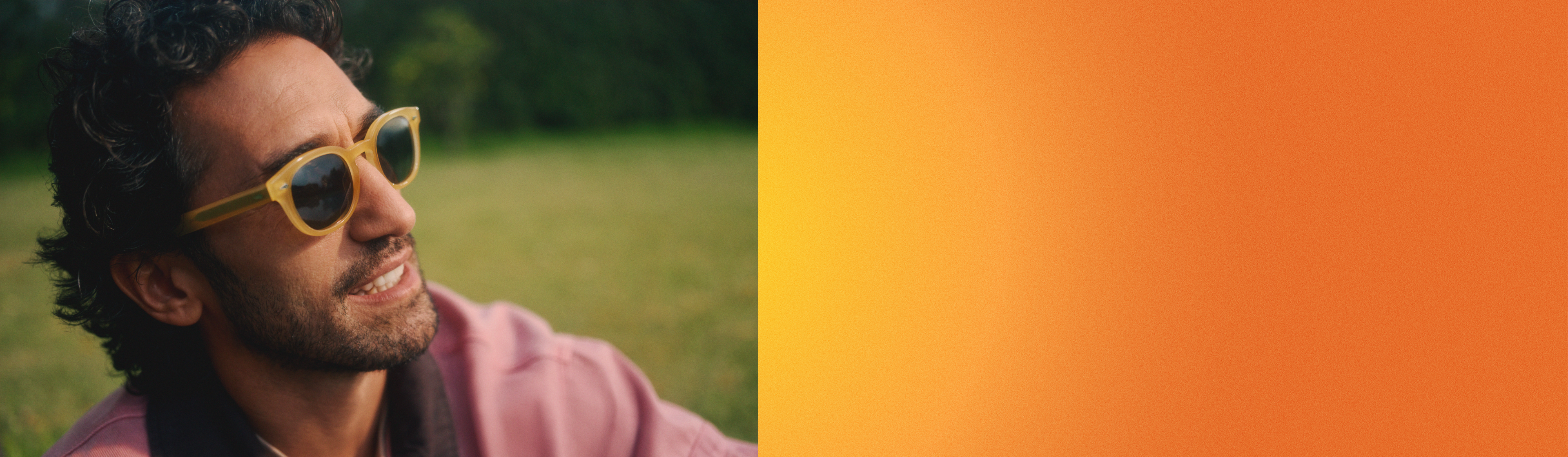 Eine Person mit gelber Sonnenbrille sitzt lächelnd draußen auf dem Rasen.