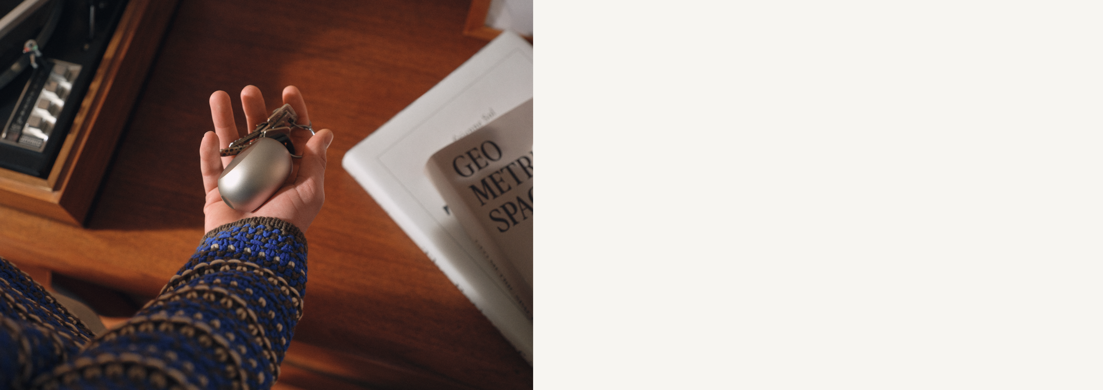 Eine Person mit gemustertem blauem Ärmel hält ein silbernes Ladegerät über einem Holztisch, in der Nähe liegt ein Buch mit dem Titel „GEOMETRY SPACE“.