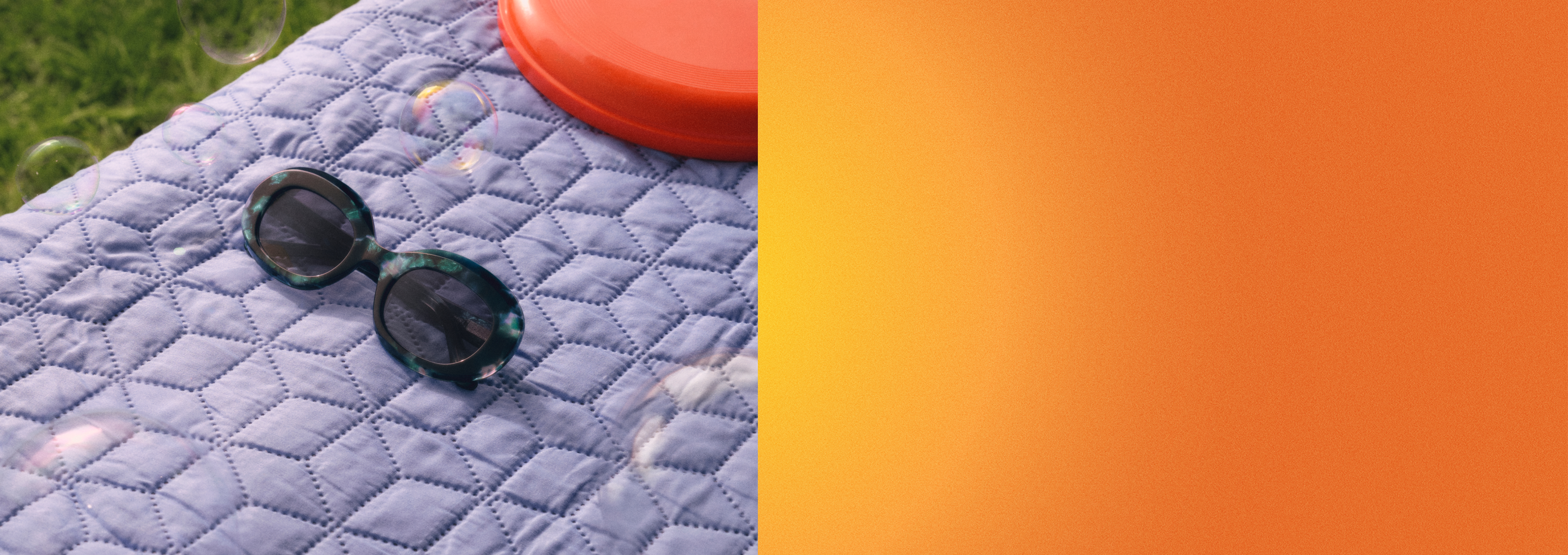 Sonnenbrille und orangefarbener Frisbee auf einer blauen Steppdecke mit Seifenblasen, die in der Nähe schweben, auf Gras liegend.