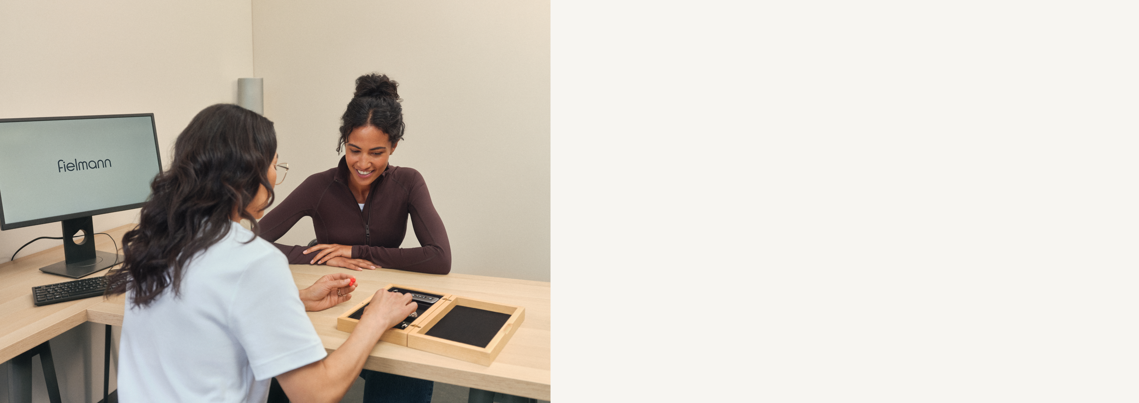 Zwei Personen sitzen an einem Schreibtisch mit einem Computer und einem Tablet und führen ein Gespräch. Eine Person zeigt auf das Tablet.