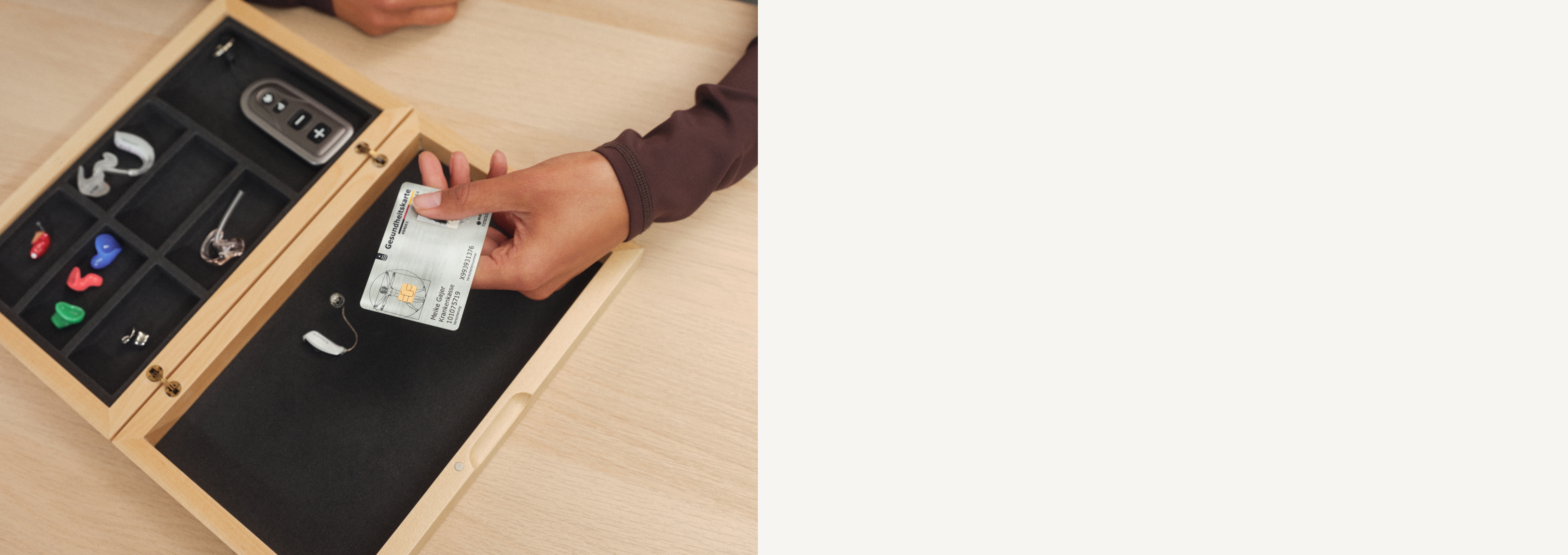 Eine Person legt eine Krankenkassenkarte in einen Holz-Organizer mit verschiedenen Fächern, die Schlüssel und bunte Gegenstände enthalten, auf einer hellen Holzoberfläche.