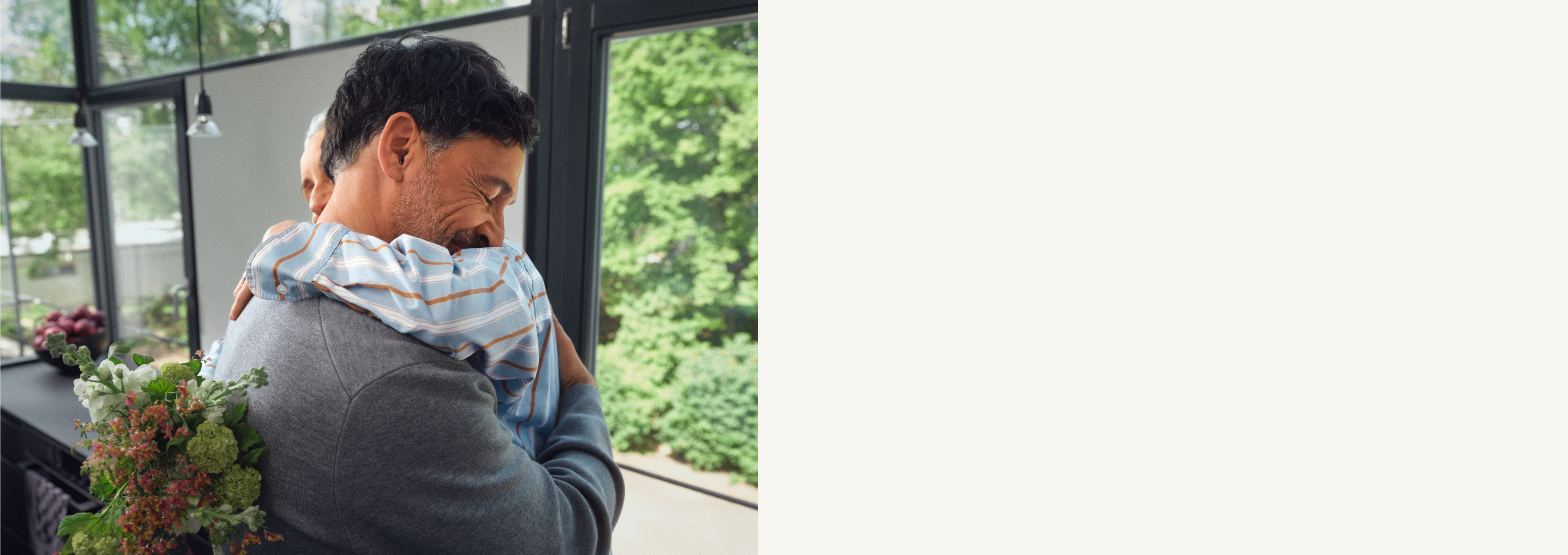 Zwei Personen umarmen sich. Eine Person hält einen Blumenstrauß in der Hand.