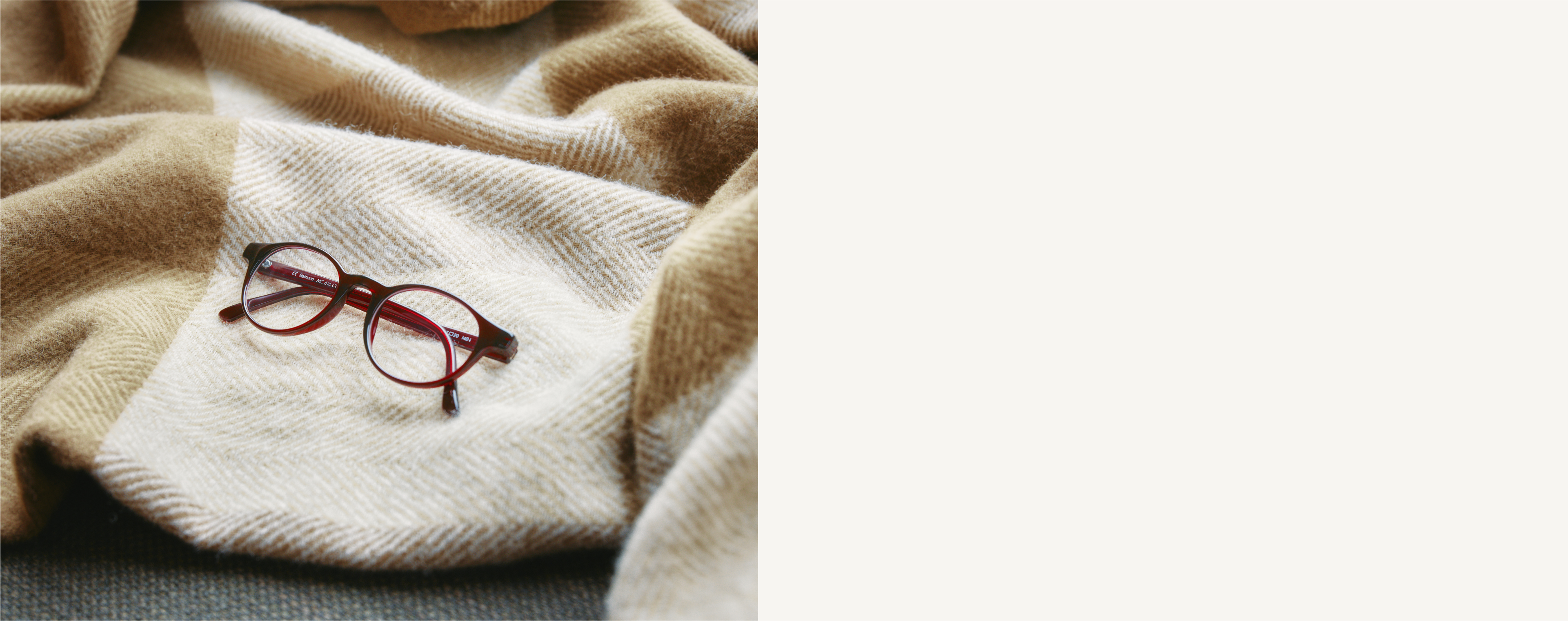Rote Brille auf einer beige-weißen Decke mit Fischgrätenmuster, rechts davon ein einfarbiger weißer Hintergrund.