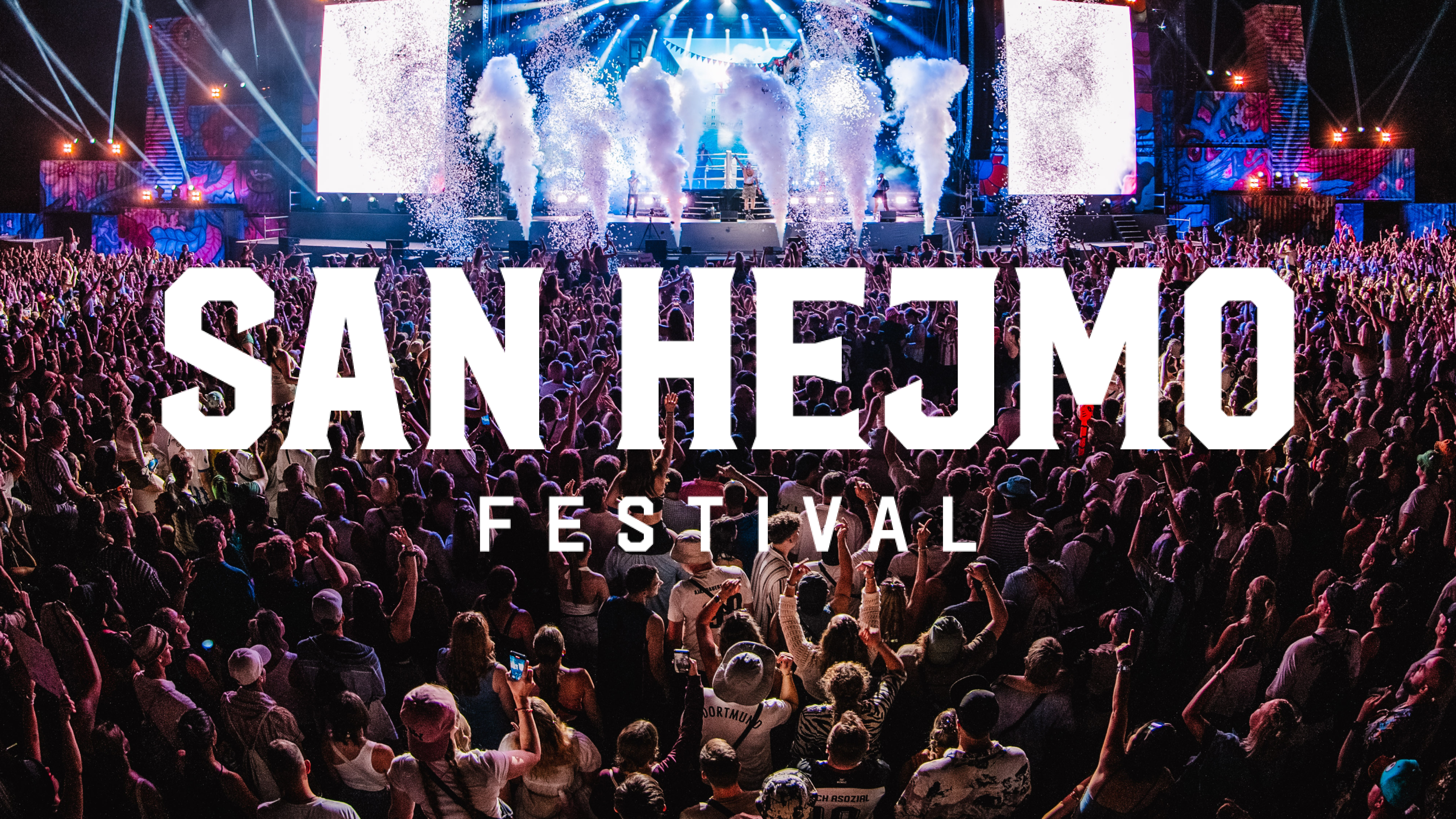 Eine große Menschenmenge genießt ein lebhaftes Musikfestival mit grellen Lichtern und Raucheffekten auf der Bühne, auf der der Schriftzug „SAN HEJMO FESTIVAL“ zu sehen ist.