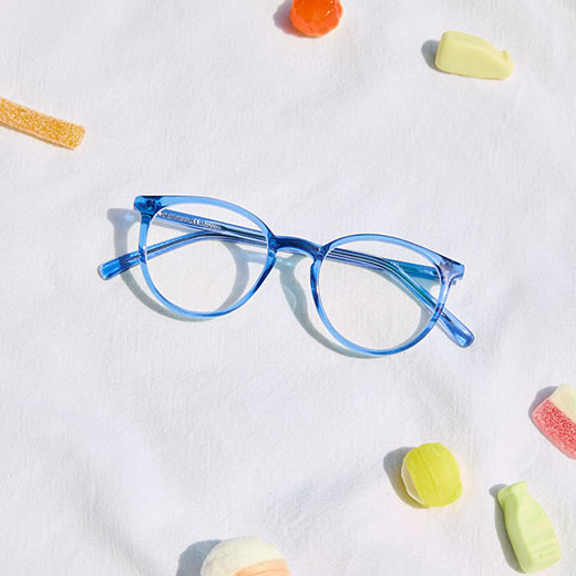 Blaue runde Brille auf einer weißen Oberfläche, umgeben von verschiedenen bunten Süßigkeiten.