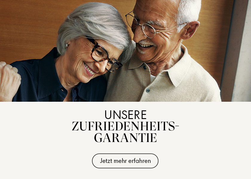 Ein älteres Ehepaar, beide tragen eine Brille und lächeln, mit dem Text „Unsere Zufriedenheits-Garantie” und einem Button mit der Aufschrift „Jetzt mehr erfahren”.
