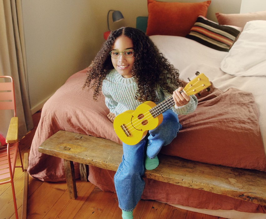 Mädchen mit Brille spielt auf einer kleinen gelben Gitarre.