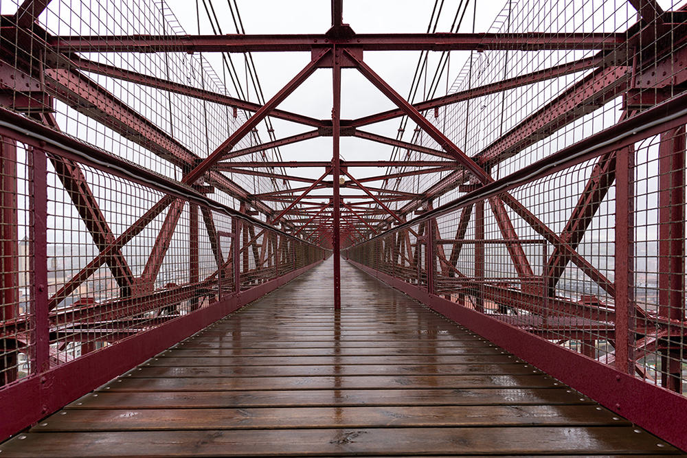 Symmetrische Ansicht einer roten Metallbrücke mit Holzplanken, mit Gitterwänden und einem nebligen Hintergrund.