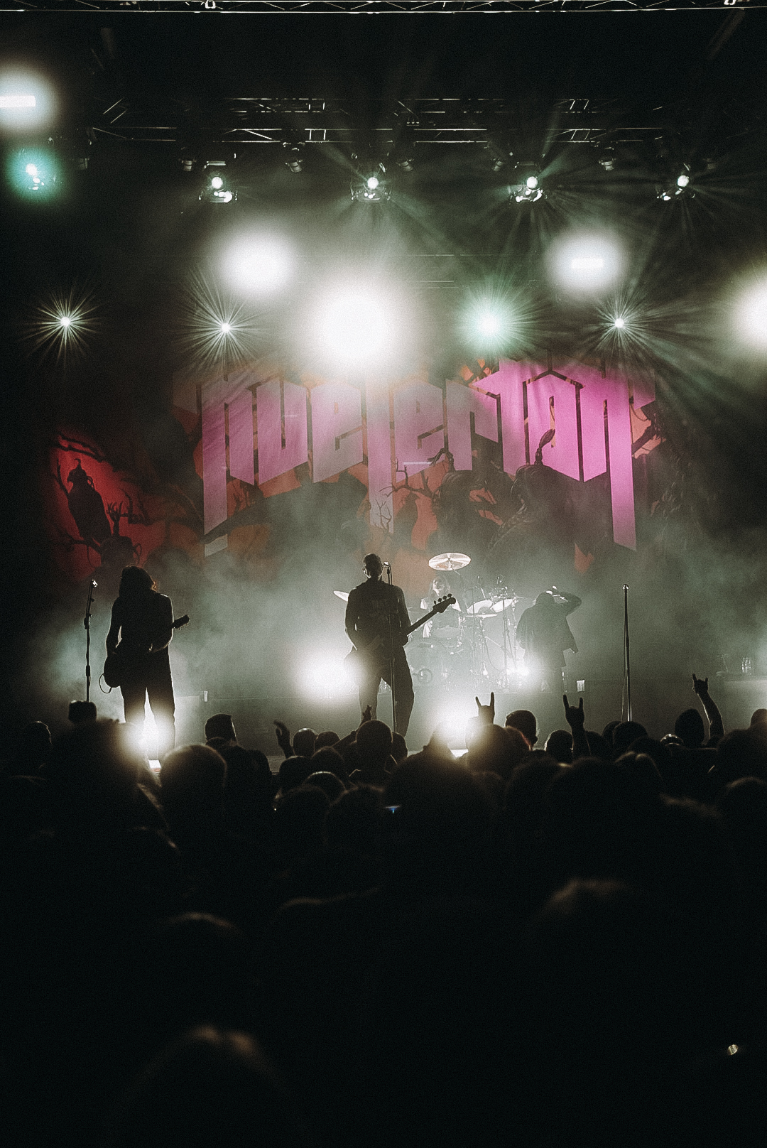 Eine Band spielt silhouettenhaft auf der Bühne, umgeben von grellen Lichtern und einer riesigen ‚Powertrip‘-Backdrop. Vor der Bühne tobt die Menge, jubelnd und voll Adrenalin.